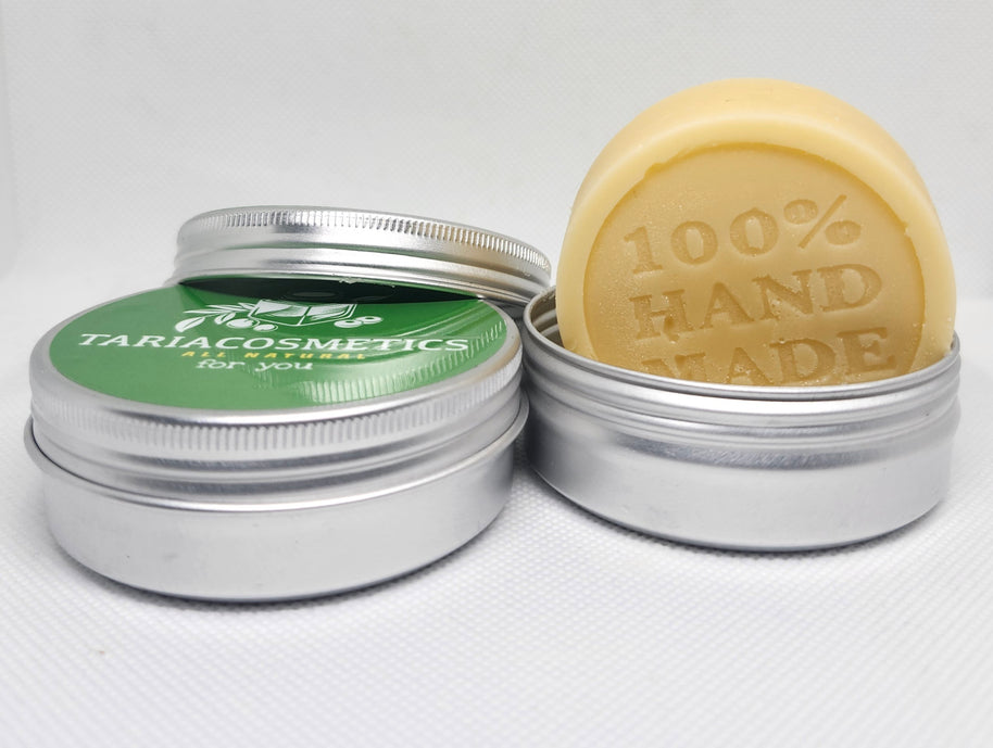 Two silver metal tins for TariaCosmetics; one is closed with a green label and the other is open to reveal a tan lotion bar with the words 