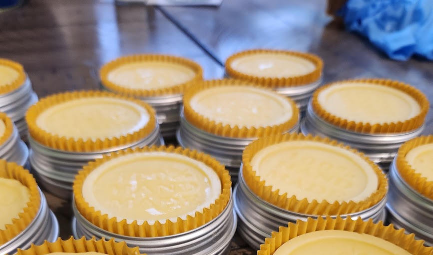Stacks of yellow lotion bars with yellow cupcake liners in tins on a metal surface.