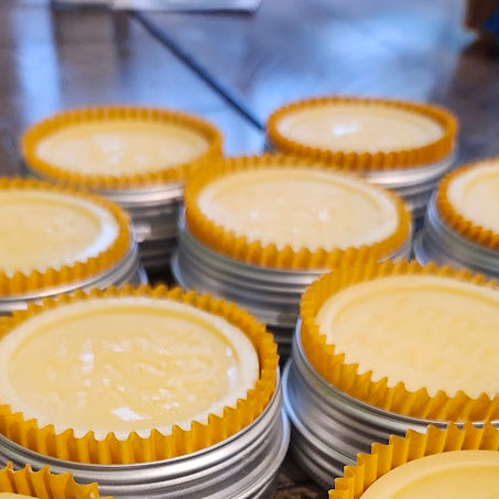 Stacks of yellow lotion bars with yellow cupcake liners in tins on a metal surface.