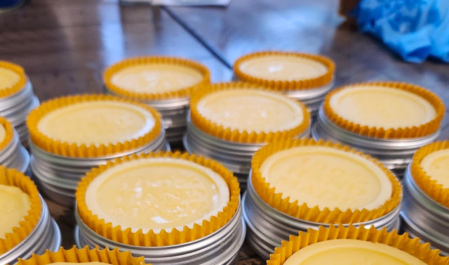 Stacks of yellow lotion bars with yellow cupcake liners in tins on a metal surface.