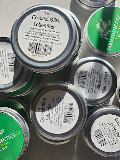 Tins of coconut olive lotion bars with labels on a reflective surface