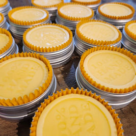 Stacks of tins filled with lotion bars with gold cupcake liners on a wooden surface.