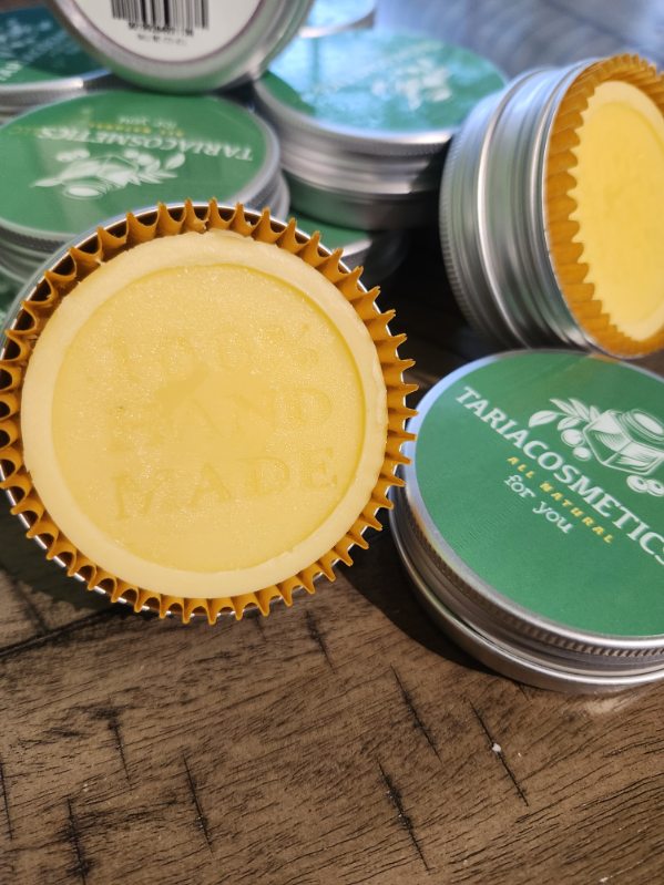 Stacks of lotion bars in tins with yellow bars in them surrounded by gold cookie cups on a wooden surface