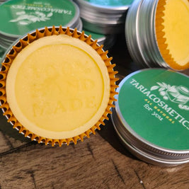 Stacks of lotion bars in tins with yellow bars in them surrounded by gold cookie cups on a wooden surface