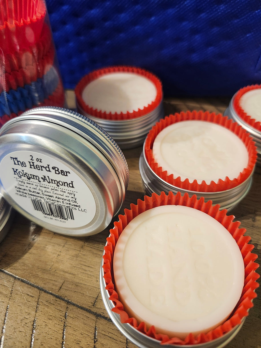 White lotion bars with red liners in a metal tin with a ton of kokum almond lotion bar in the foreground.