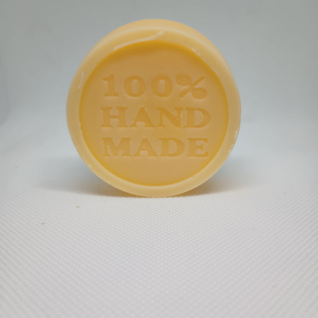 A tan, circular lotion bar is stamped with the words "100% HAND MADE".