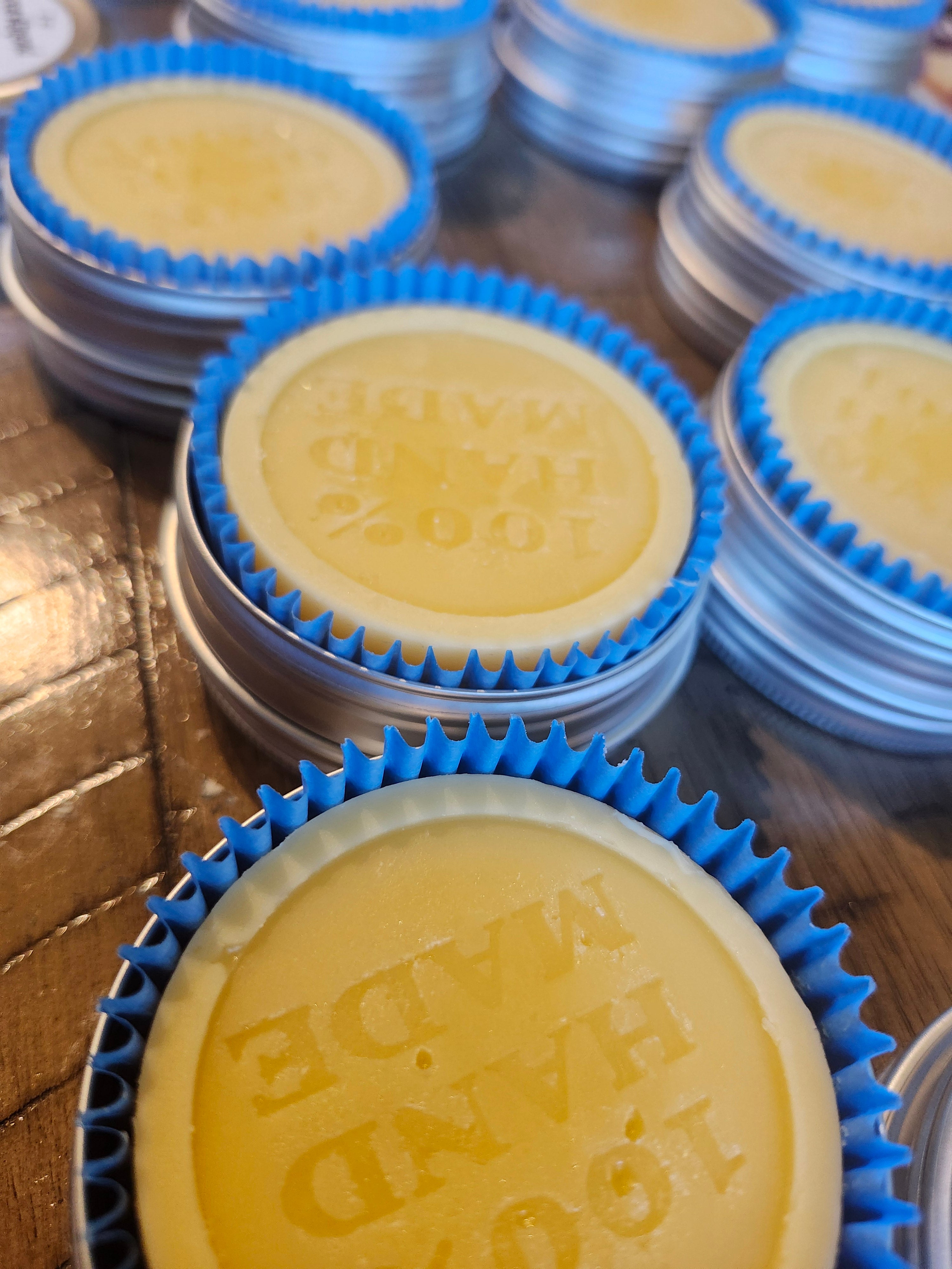 Yellow lotion bars with blue wrappers in a tin on a wooden surface