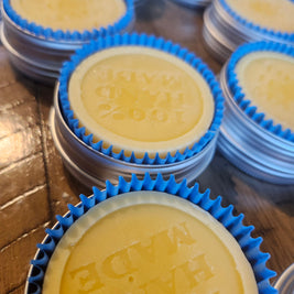 Yellow lotion bars with blue wrappers in a tin on a wooden surface