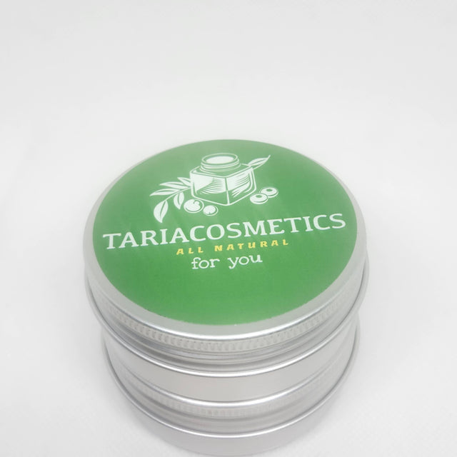 A metal cosmetic tin with a green circular label on the lid featuring the brand name TariaCosmetics  an ALL NATURAL FOR YOU tagline and an illustration of a jar and leaves