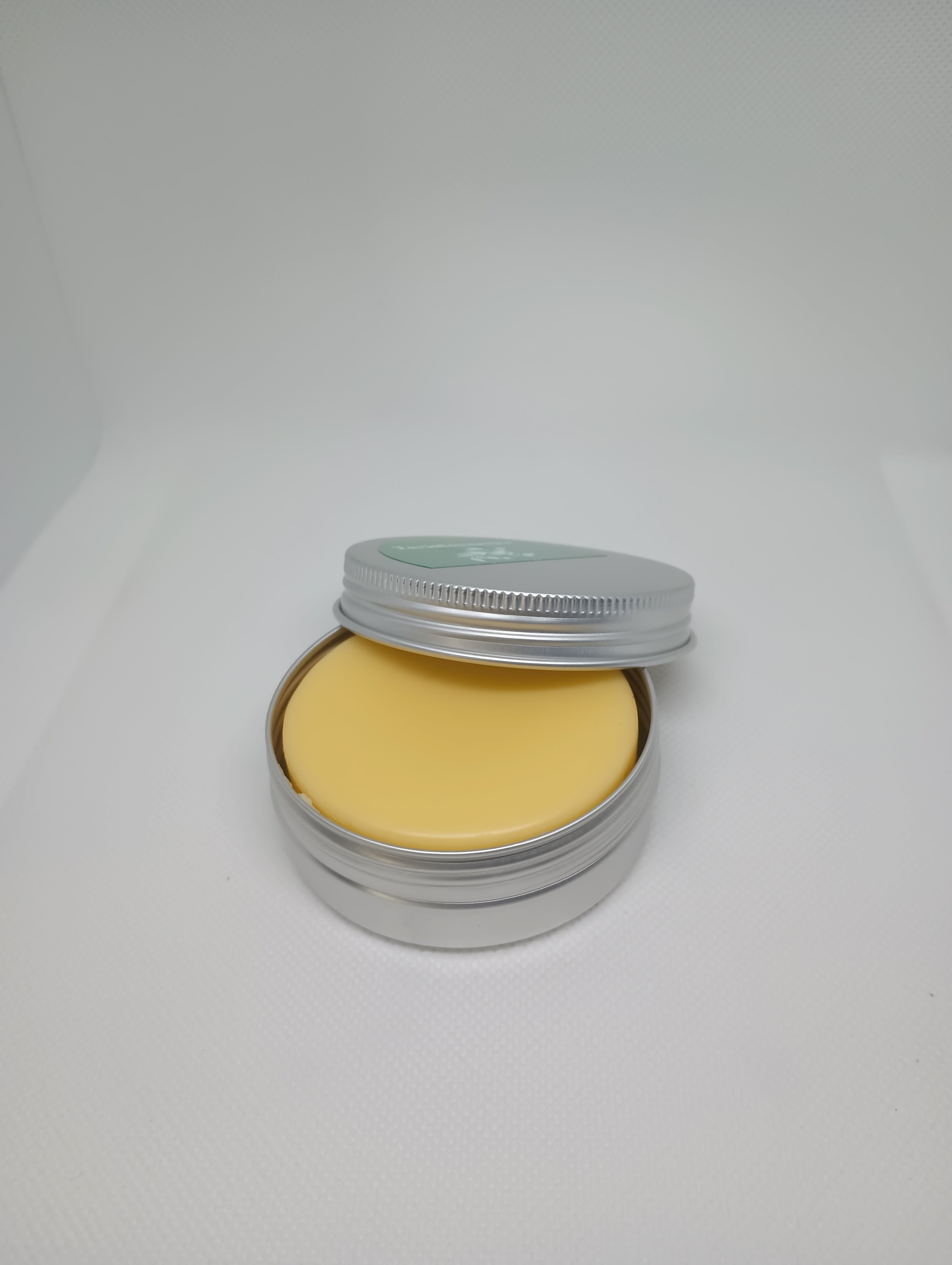 A solid lotion bar inside an open metal tin with a light yellow color, suggesting a creamy texture.