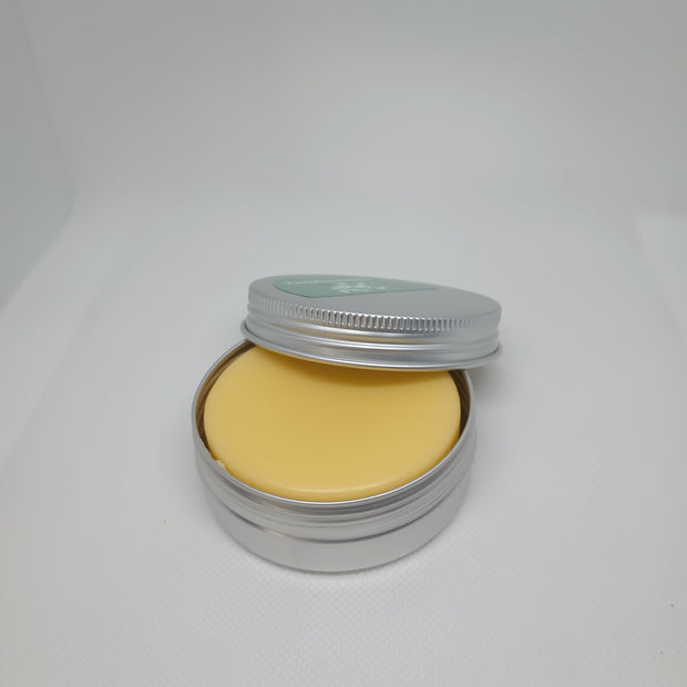 A solid lotion bar inside an open metal tin with a light yellow color, suggesting a creamy texture.